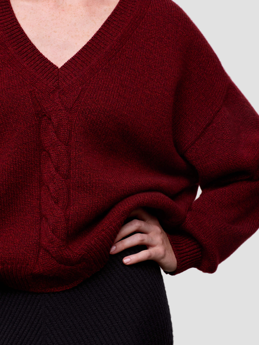 woman wearing a red chunky v-neck cashmere sweater and black cashmere skirt on a grey background