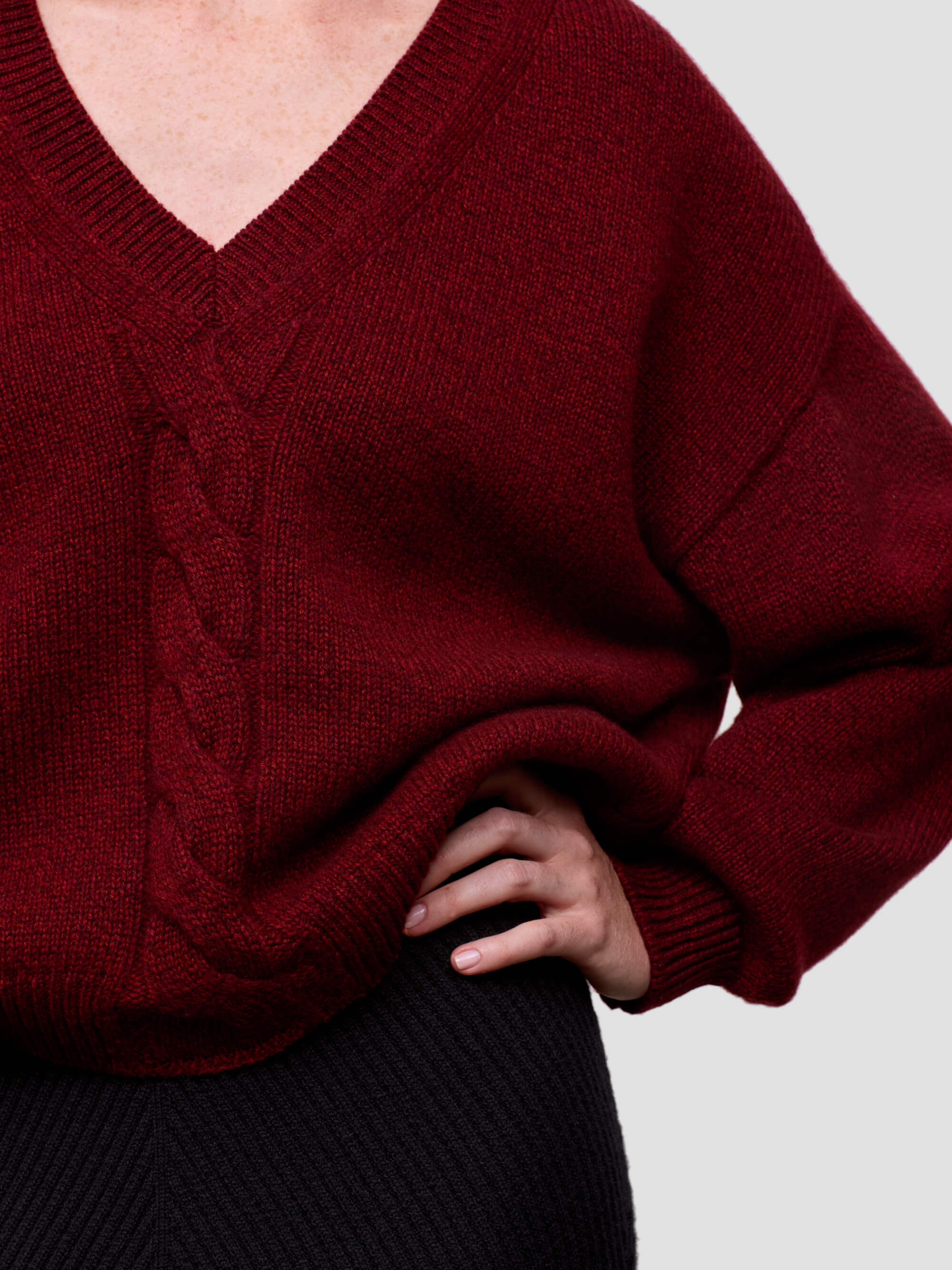 woman wearing a red chunky v-neck cashmere sweater and black cashmere skirt on a grey background
