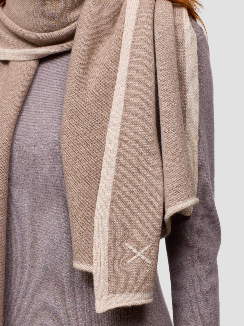 woman wearing a brown cashmere wrap with embroidered 'X' detail and grey cashmere dress on a grey background