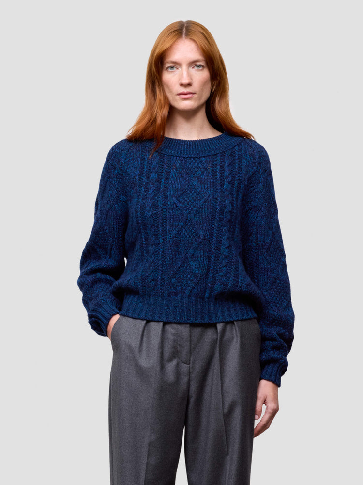 woman wearing a blue cable knit cashmere sweater and gray pants on a plain background