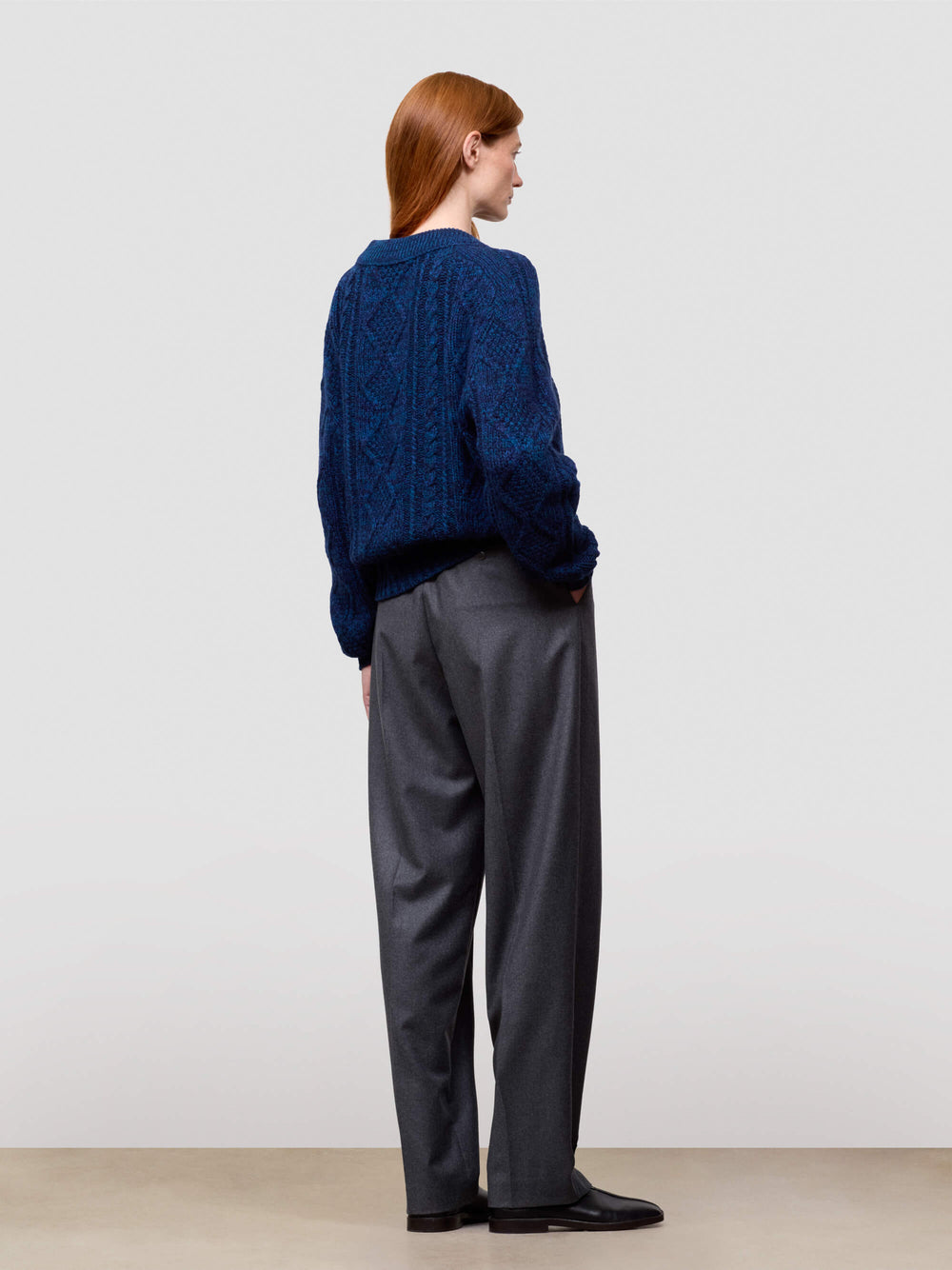 woman wearing a blue cable knit cashmere sweater and gray pants on a plain background