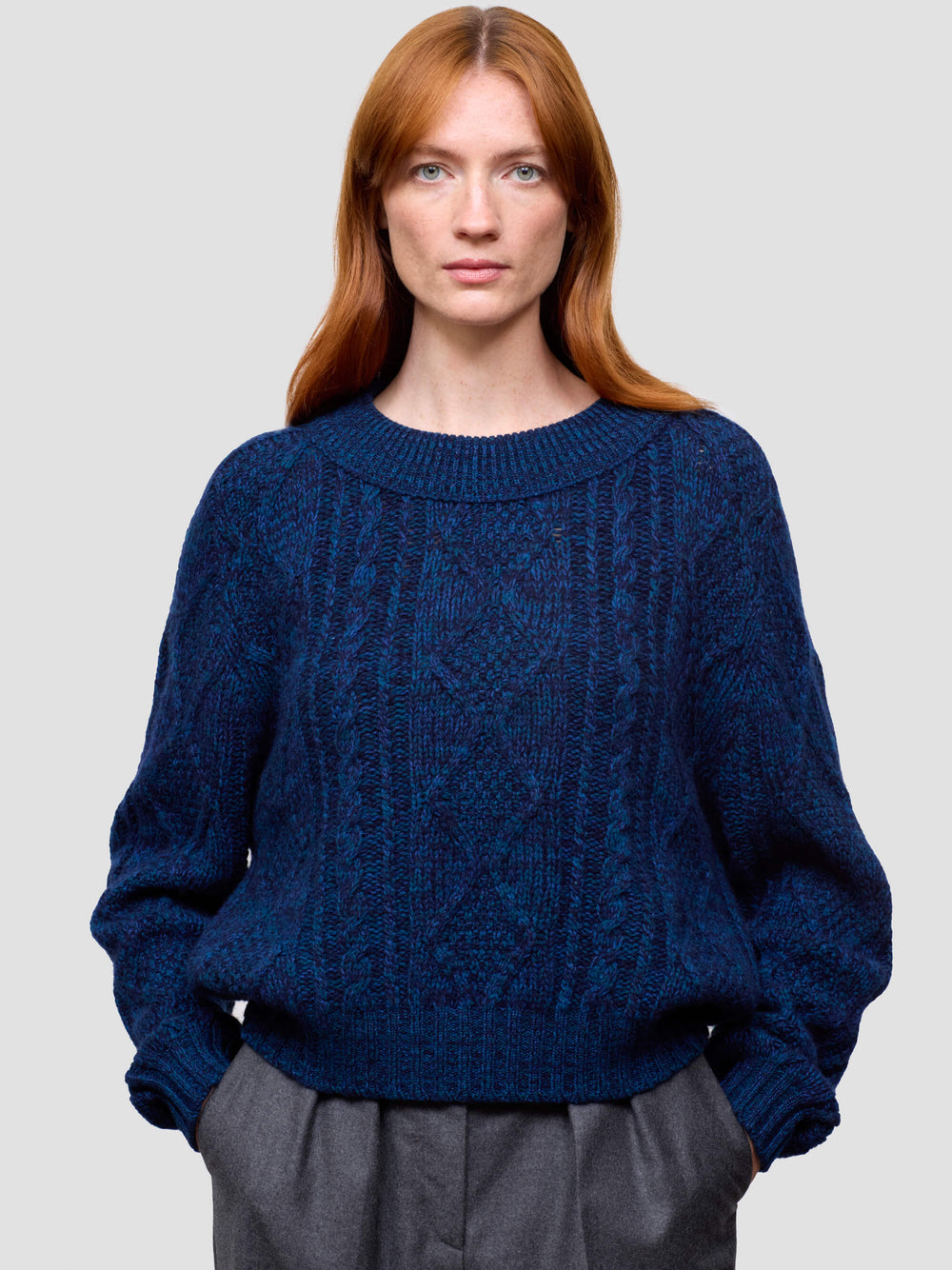 woman wearing a blue cable knit cashmere sweater and gray pants on a plain background