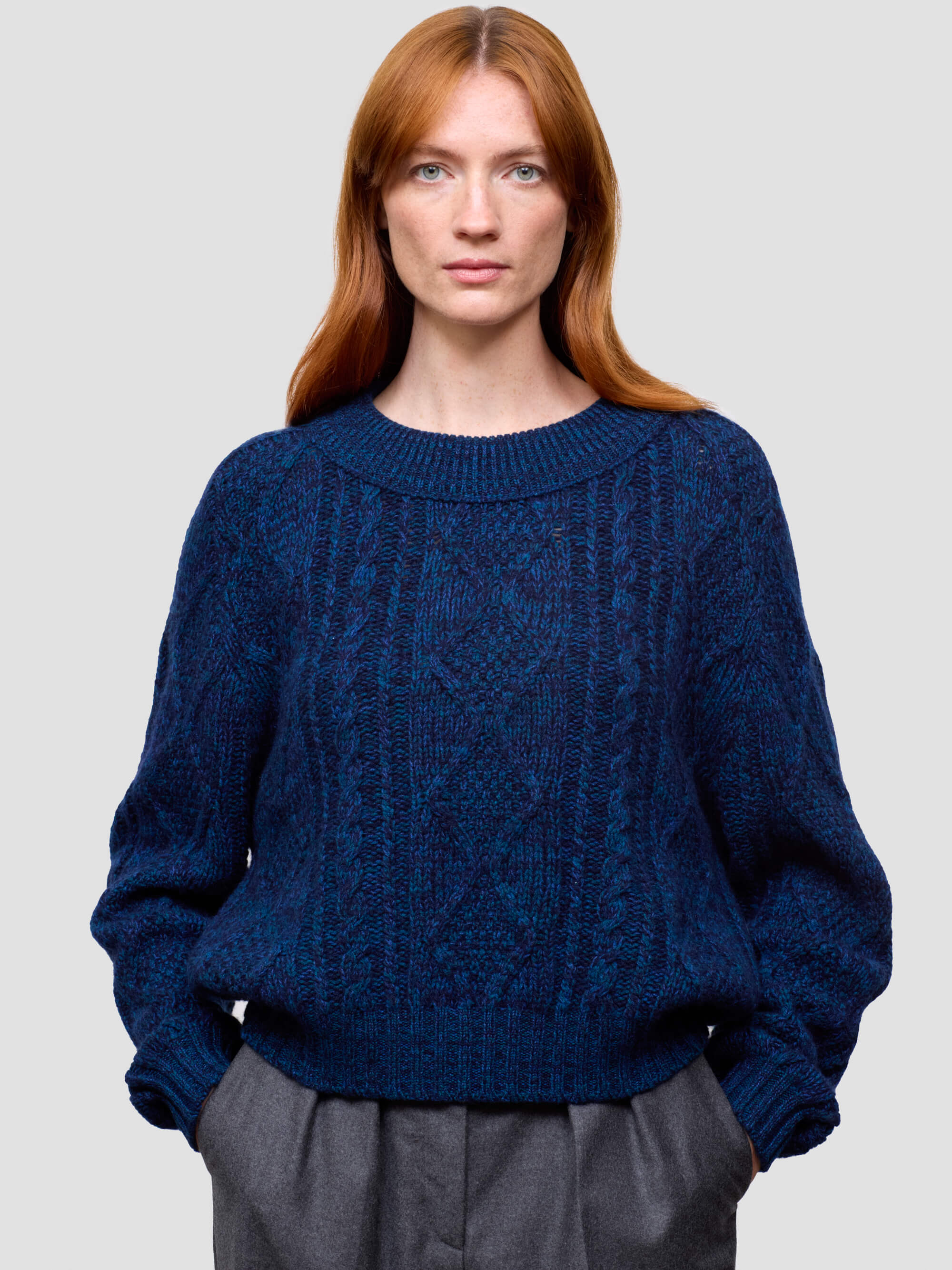 woman wearing a blue cable knit cashmere sweater and gray pants on a plain background