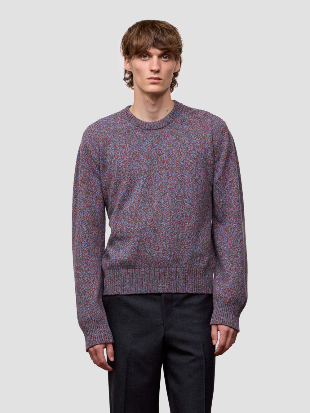 Man wearing a patterned purple cashmere sweater and black pants on a plain background