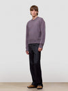 Man wearing a patterned purple cashmere sweater and black pants on a plain background