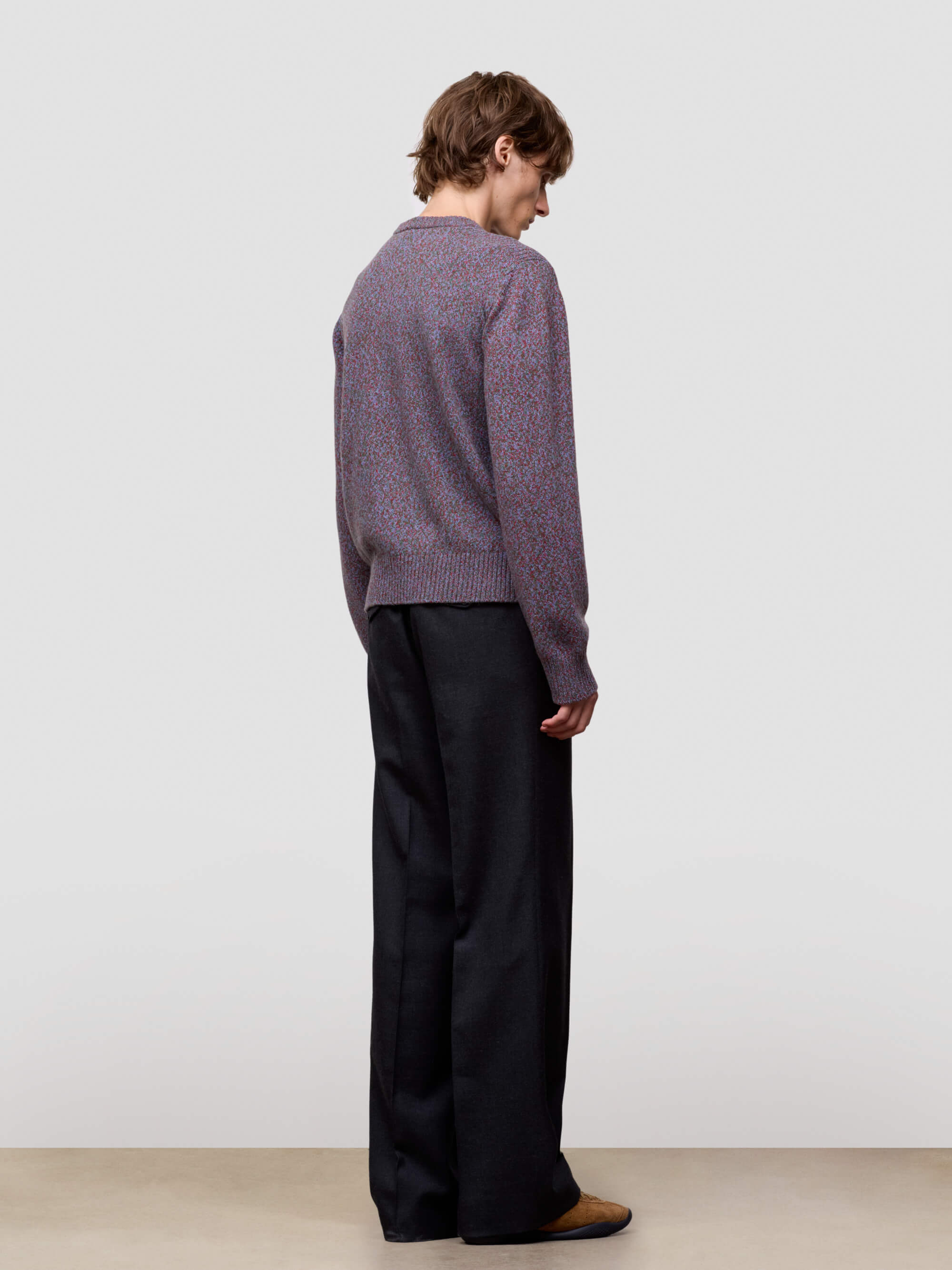 Man wearing a patterned purple cashmere sweater and black pants on a plain background