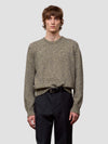 Man wearing a patterned green cashmere sweater and dark pants on a plain background