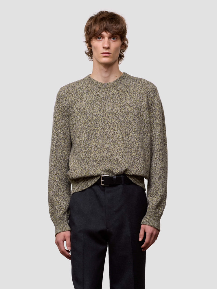Man wearing a patterned green cashmere sweater and dark pants on a plain background