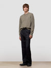Man wearing a patterned green cashmere sweater and dark pants on a plain background
