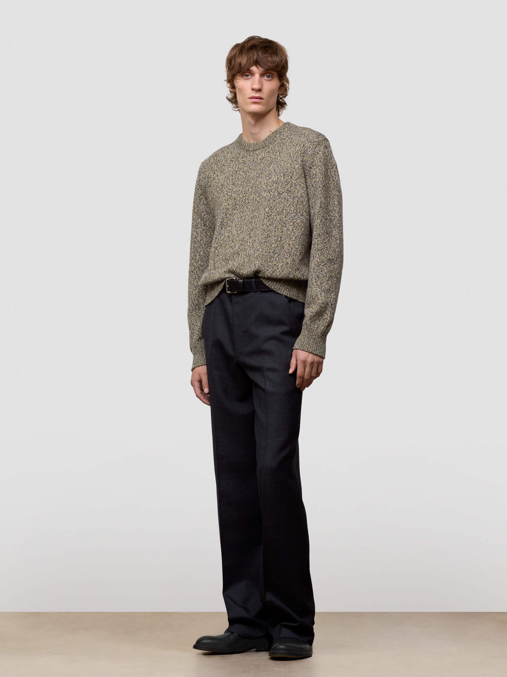 Man wearing a patterned green cashmere sweater and dark pants on a plain background