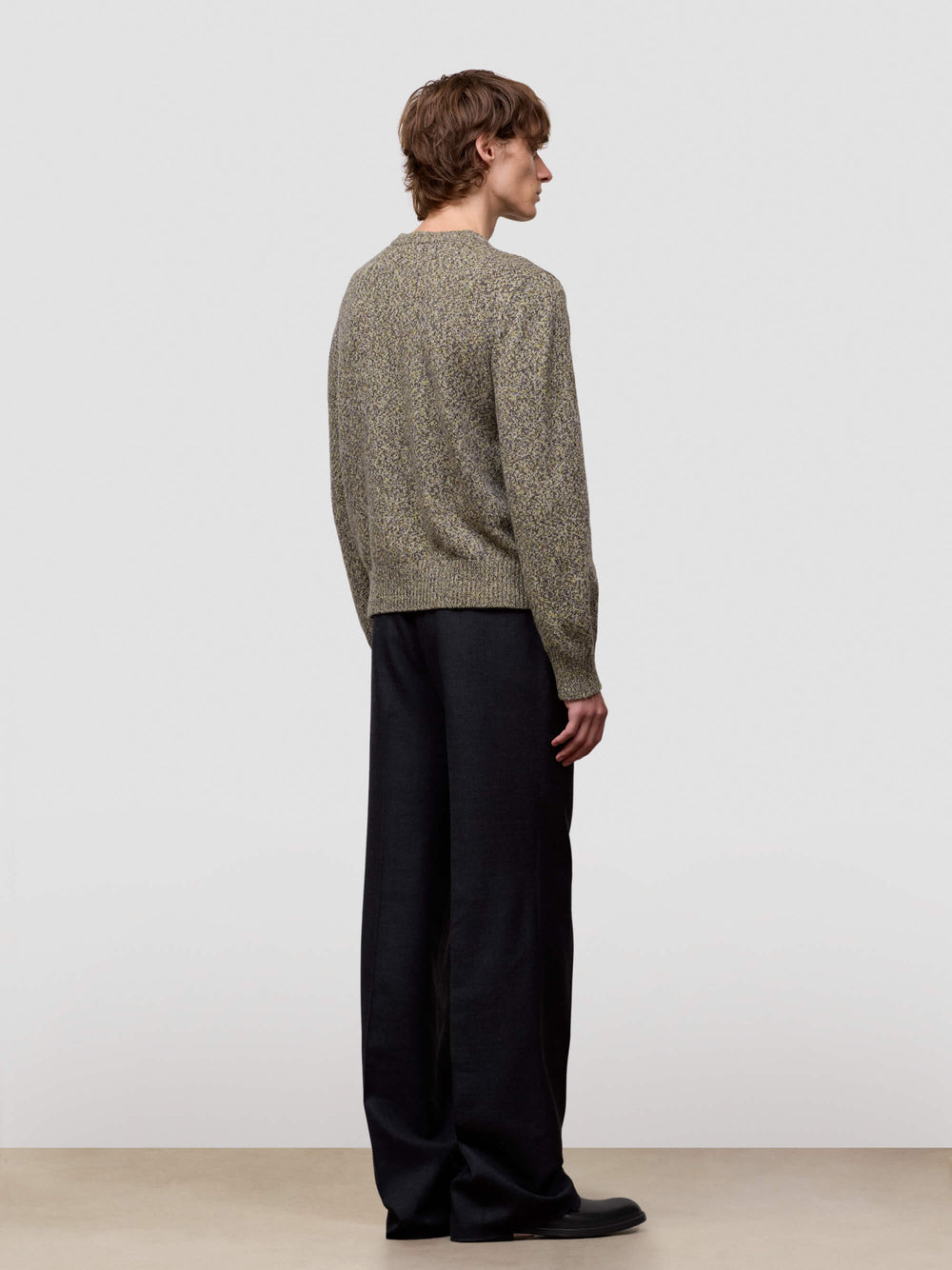 Man wearing a patterned green cashmere sweater and dark pants on a plain background