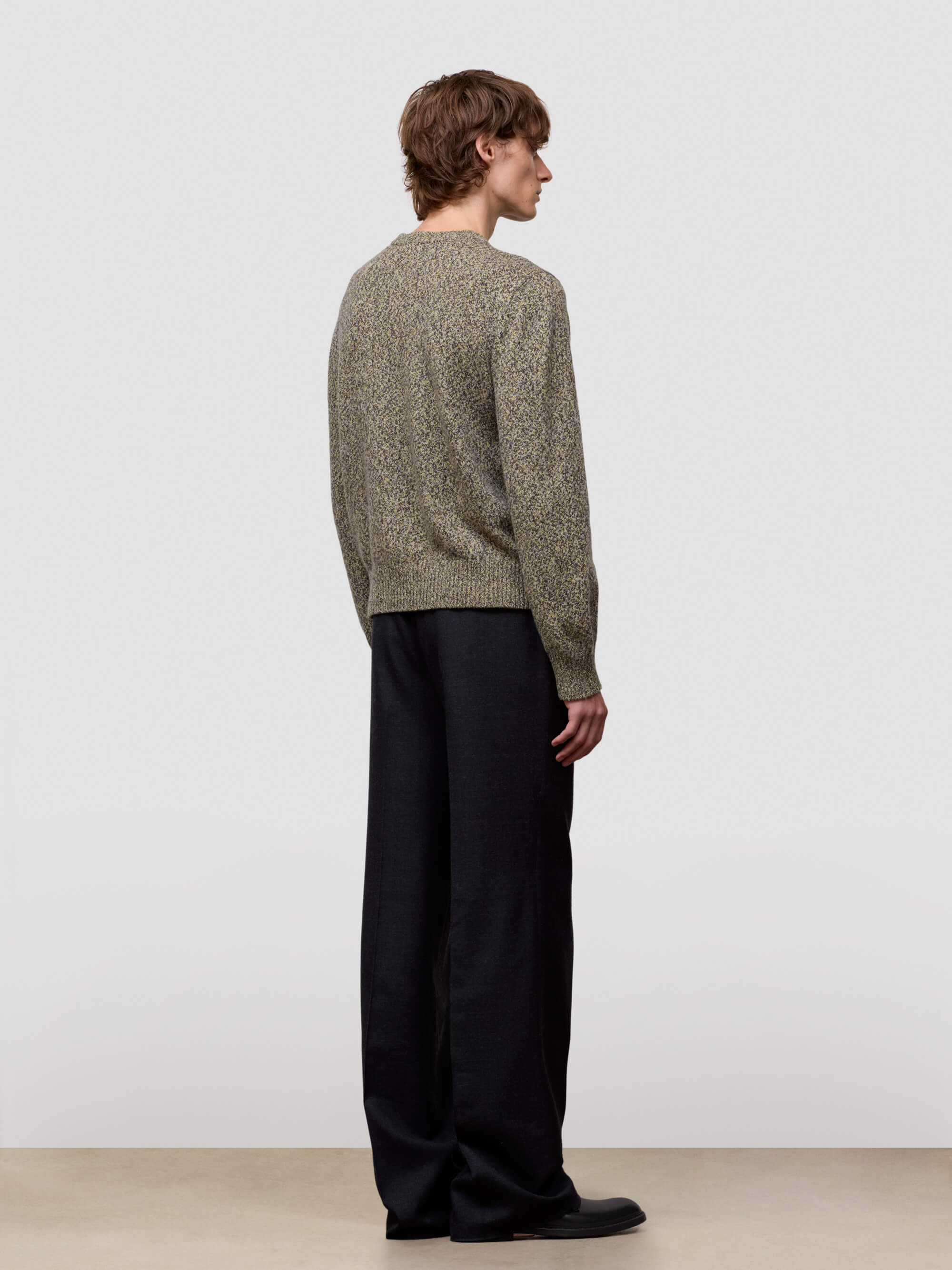 Man wearing a patterned green cashmere sweater and dark pants on a plain background