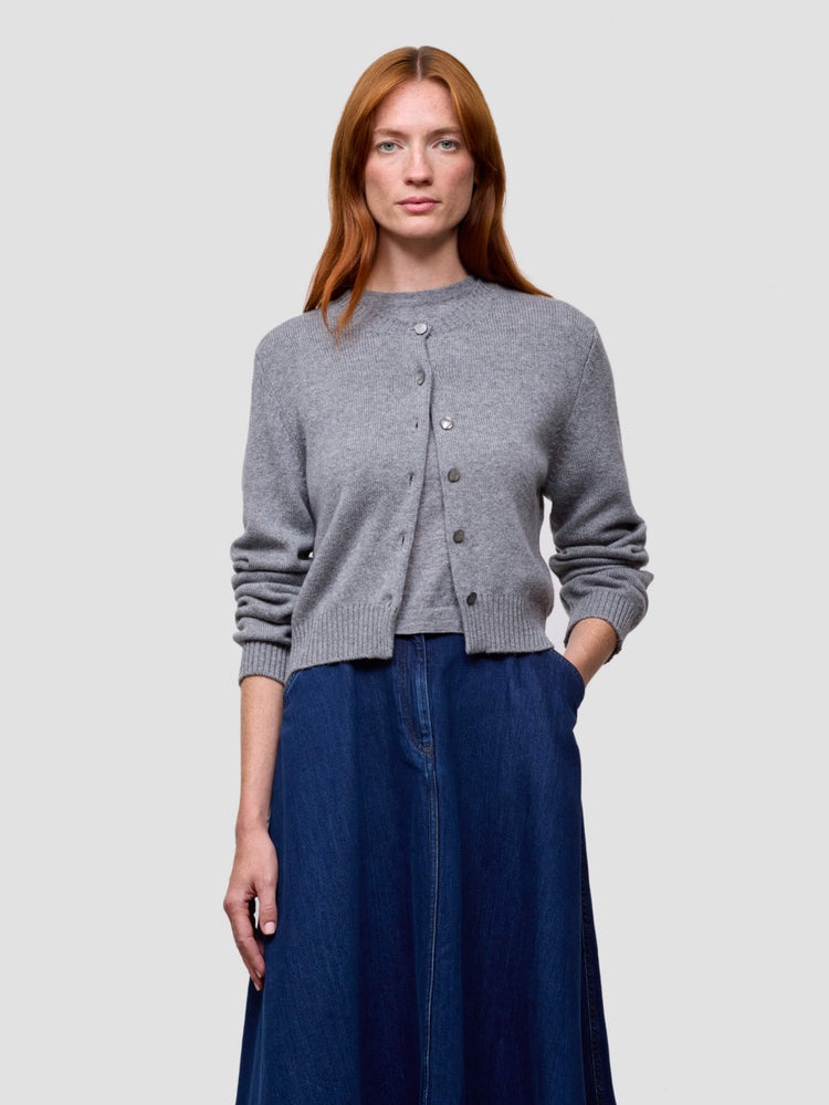 Woman wearing a gray cashmere cardigan and blue skirt on a light gray background