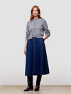 Woman wearing a gray cashmere cardigan and blue skirt and black boots on a light gray background