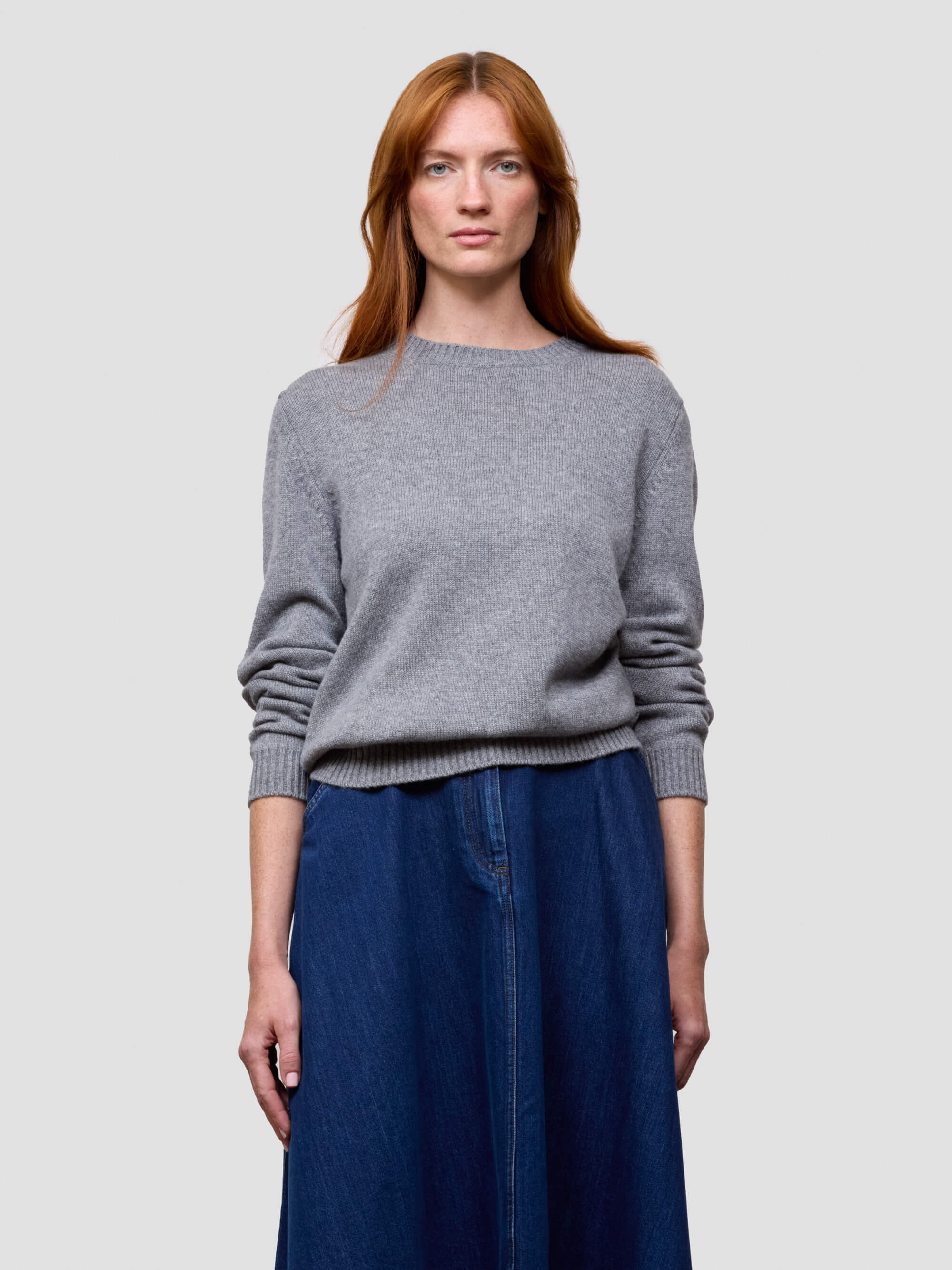 Woman wearing a gray cashmere sweater and blue skirt on a light gray background