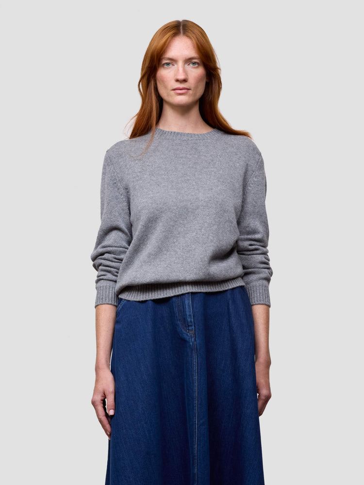 Woman wearing a gray cashmere sweater and blue skirt on a light gray background