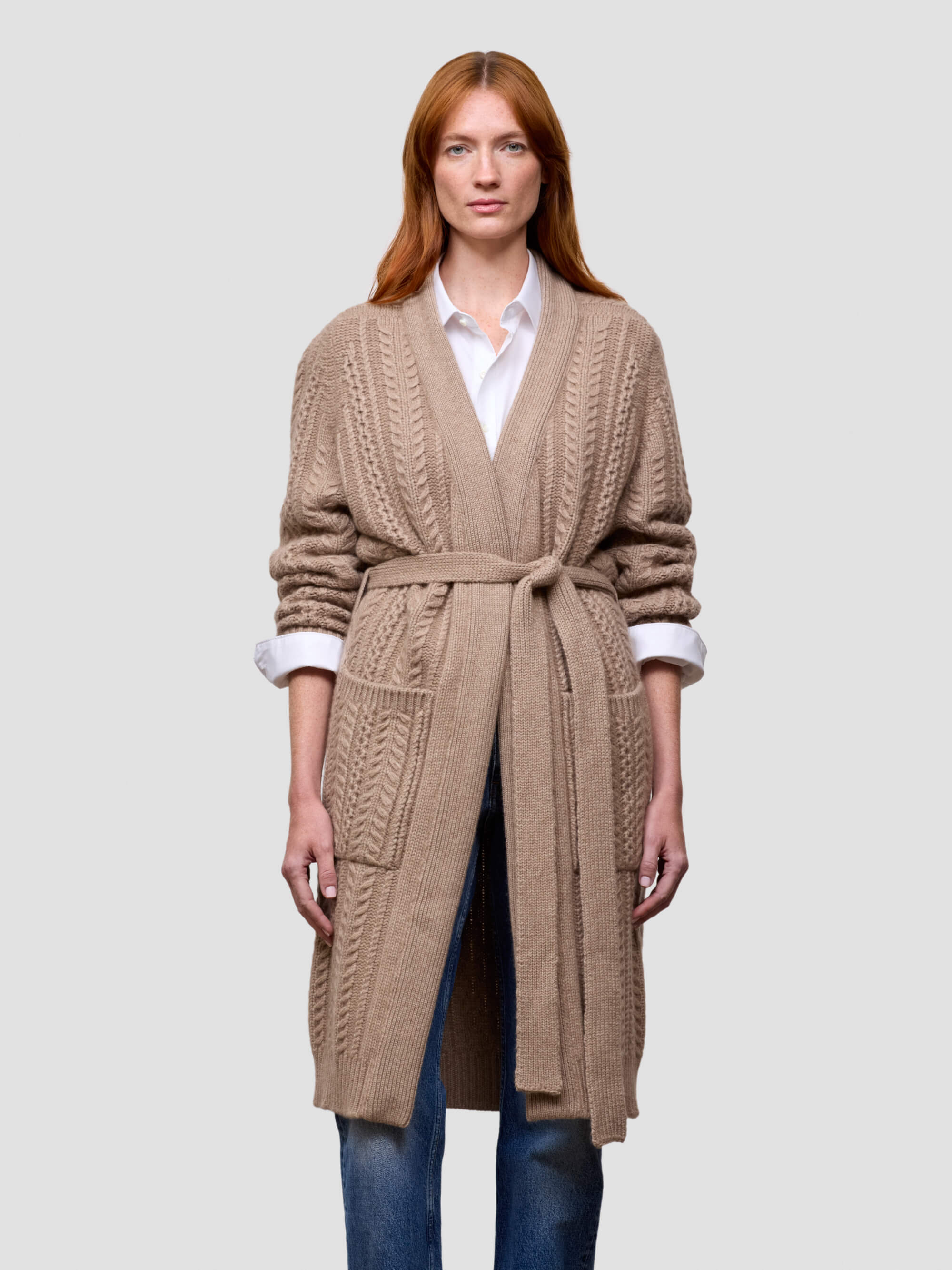 Woman wearing a beige cable knit cashmere cardigan on a light gray background