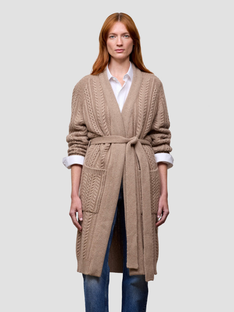 Woman wearing a beige cable knit cashmere cardigan on a light gray background
