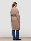 Woman wearing a long beige cable knit cashmere cardigan on a plain background