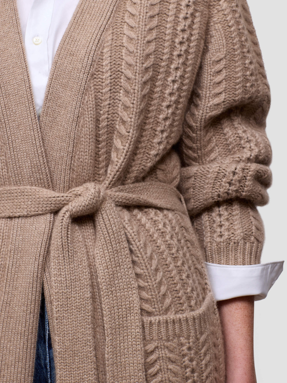 Close-up of a womanwearing a beige cable knit cardigan with a white shirt and blue jeans.