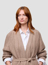 Woman wearing a beige knitted cashmere cardigan over a white shirt on a light gray background
