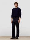 Man wearing a dark blue cable knit cashmere sweater and black pants on a light gray background