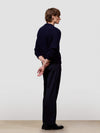 Man wearing a dark blue cable knit cashmere sweater and black pants on a light gray background