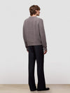 Man wearing a brown cable knit cashmere sweater and black pants on a light gray background