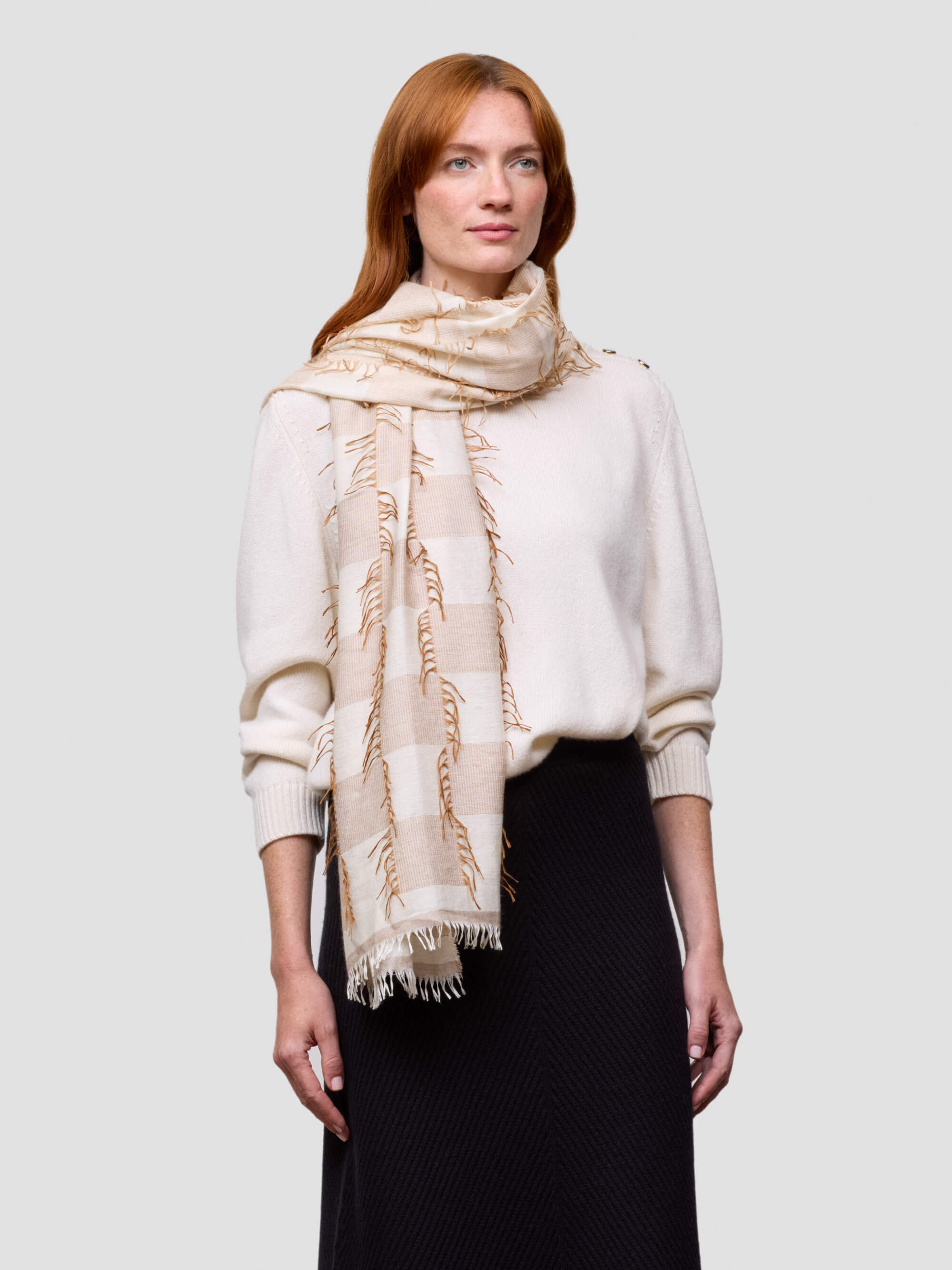Woman wearing a beige cashmere  scarf and white cashmere sweater on a light gray background