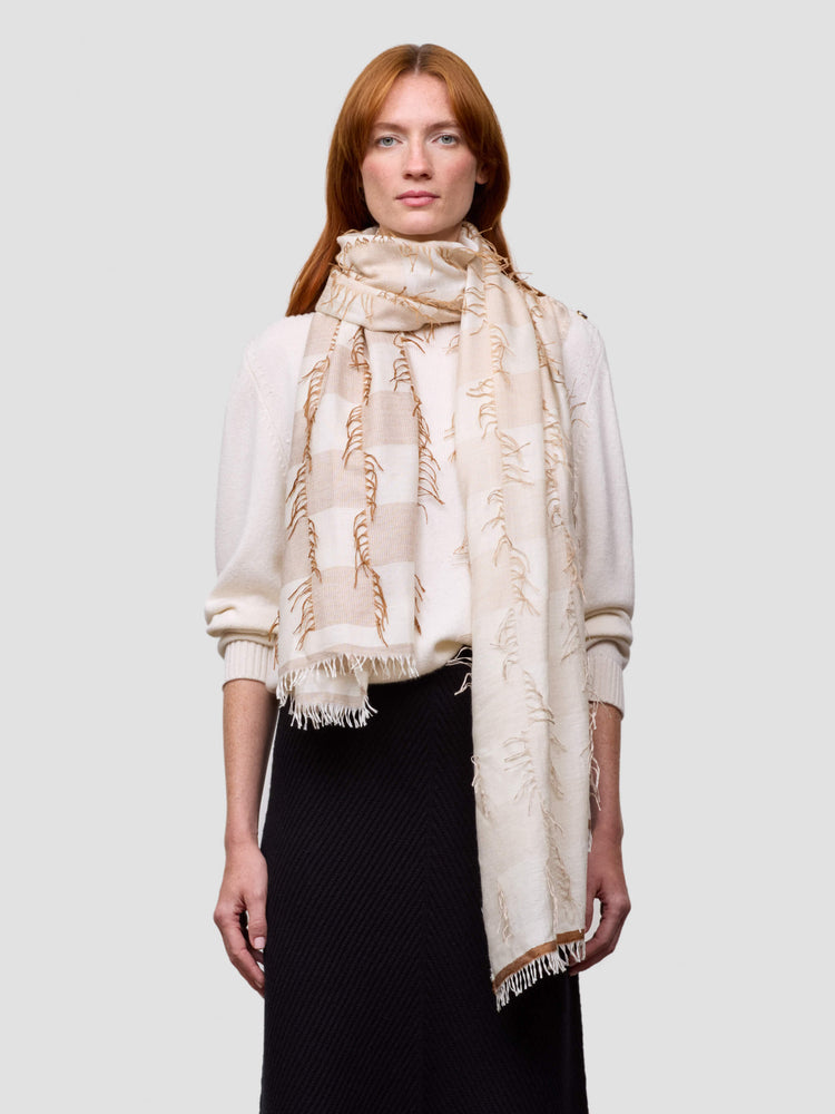 Woman wearing a beige cashmere silk scarf on a plain background