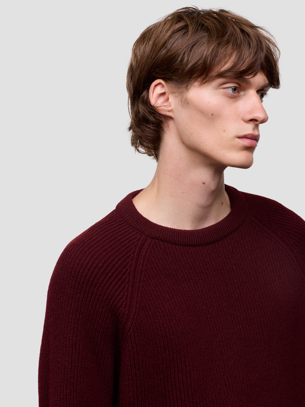 Man wearing a ribbed burgundy cashmere sweater on a light gray background