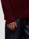 Close-up of a man wearing a burgundy sweater and dark pants on a light background