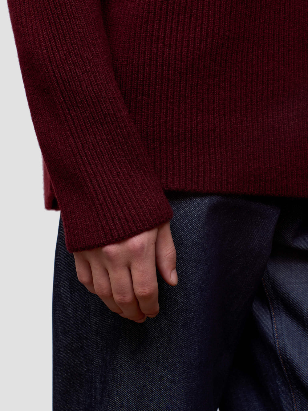 Close-up of a man wearing a burgundy sweater and dark pants on a light background