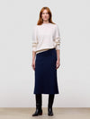 Woman wearing a white cashmere sweater and navy cashmere skirt against a plain background