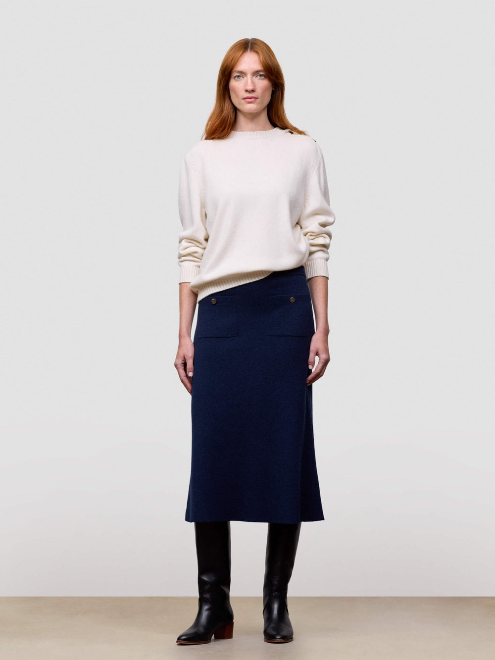 Woman wearing a white cashmere sweater and navy cashmere skirt against a plain background
