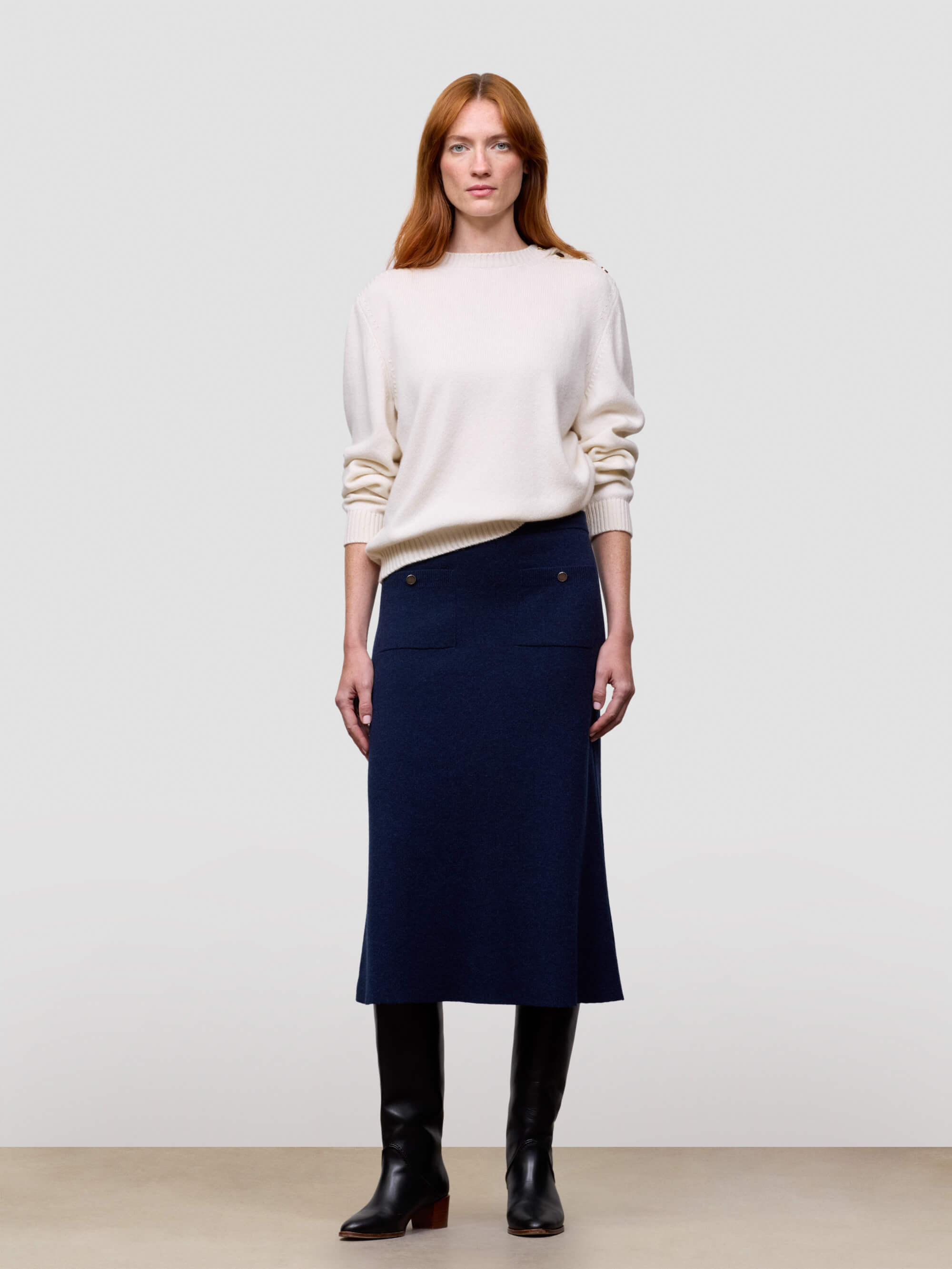 Woman wearing a white cashmere sweater and navy cashmere skirt against a plain background