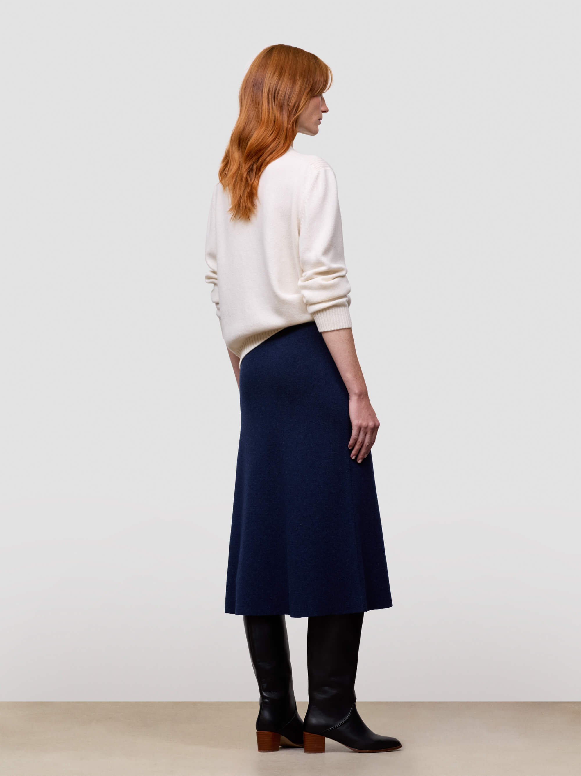 Woman wearing a white cashmere sweater and navy cashmere skirt against a plain background