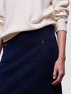 Woman wearing a white cashmere sweater and navy cashmere skirt against a plain background