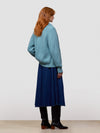 Woman wearing a teal knitted cashmere cardigan over a blue dress and black boots on a light gray background