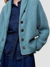 woman wearing a teal ribbed cashmere cardigan over a blue denim shirt on a plain background