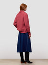 Woman wearing a red cashmere cardigan, blue dress, and black boots on a white background