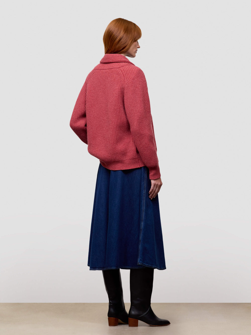 Woman wearing a red cashmere cardigan, blue dress, and black boots on a white background