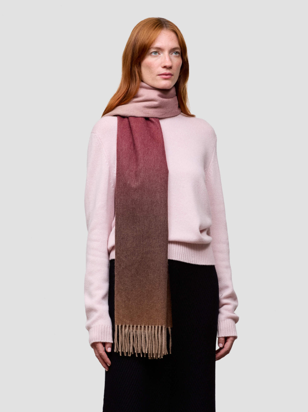 Woman wearing a pink cashmere sweater and a gradient cashmere scarf on a white background