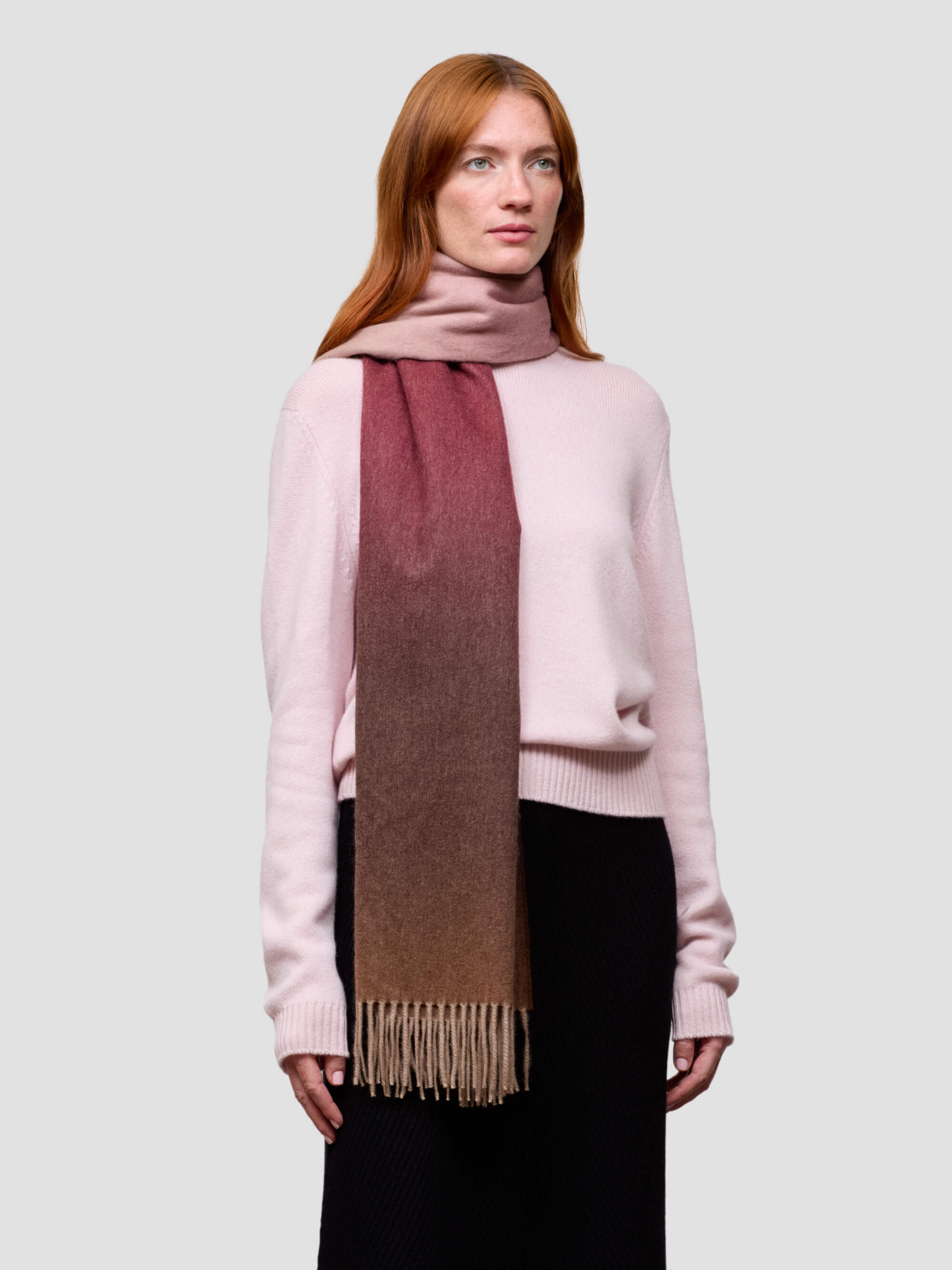 Woman wearing a pink cashmere sweater and a gradient cashmere scarf on a white background