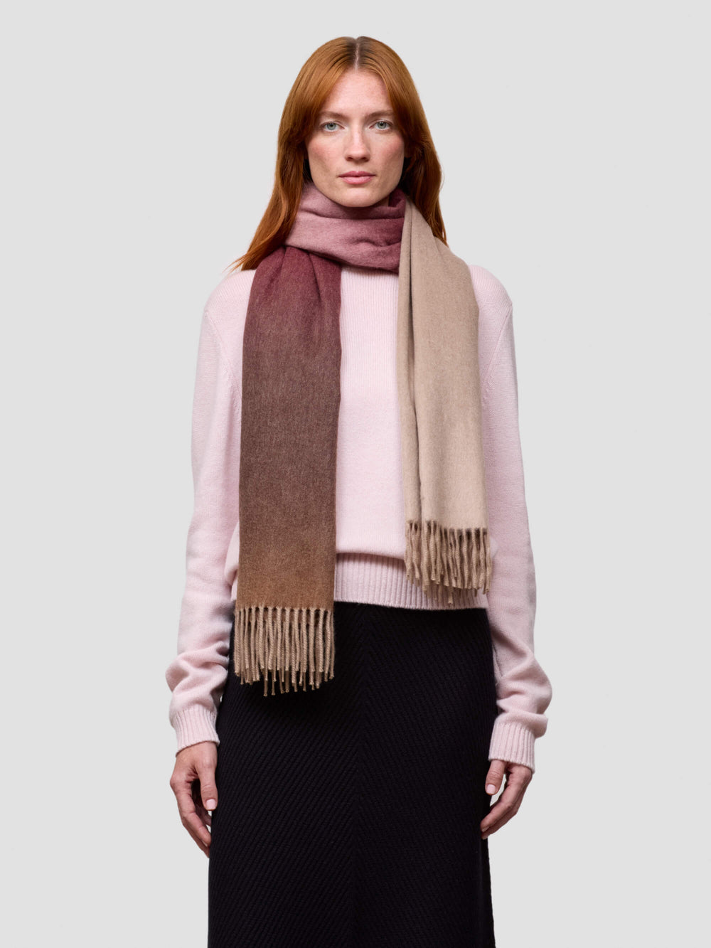 Woman wearing a pink cashmere sweater and a pink gradient cashmere scarf on a white background