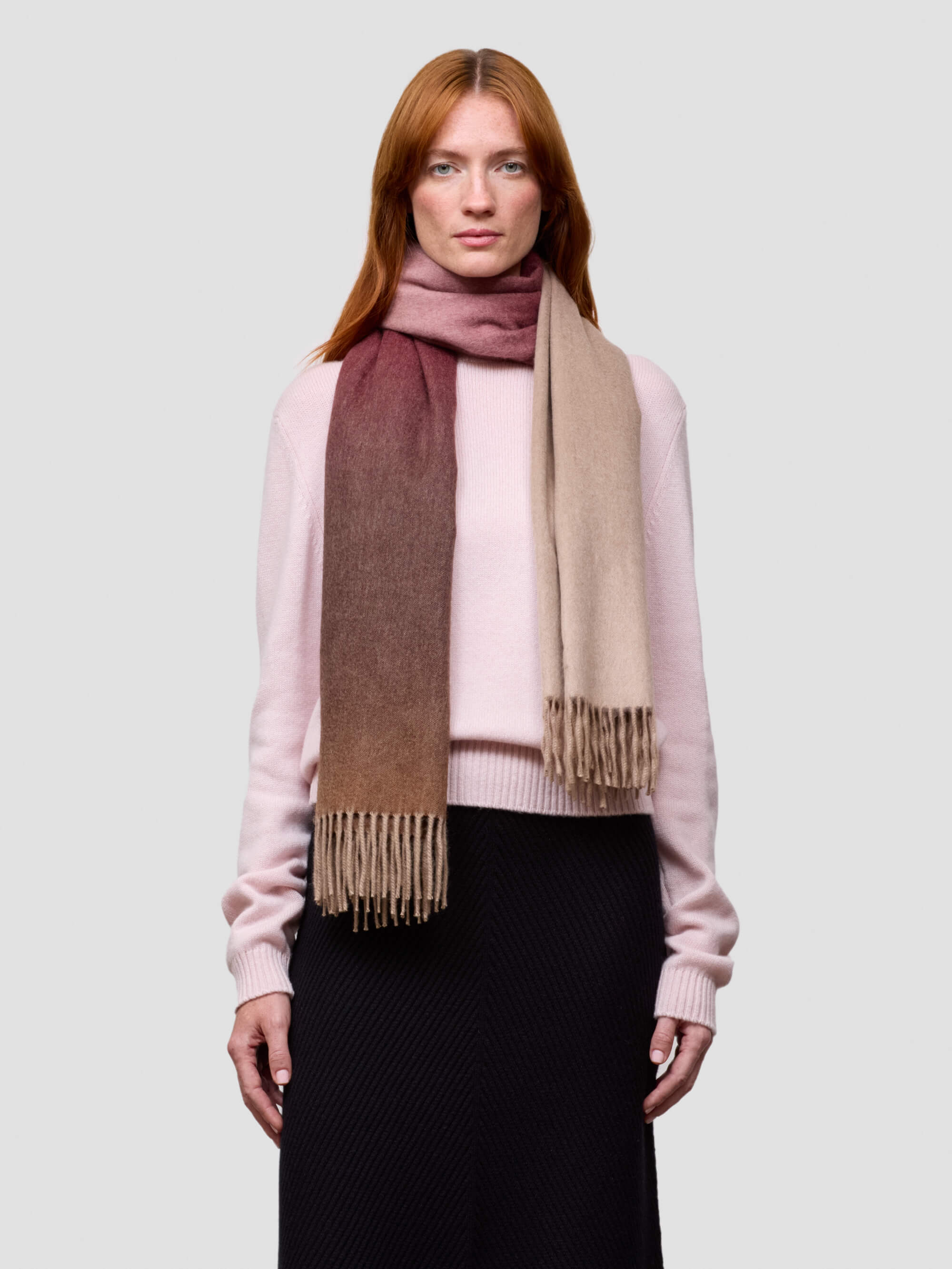 Woman wearing a pink cashmere sweater and a pink gradient cashmere scarf on a white background