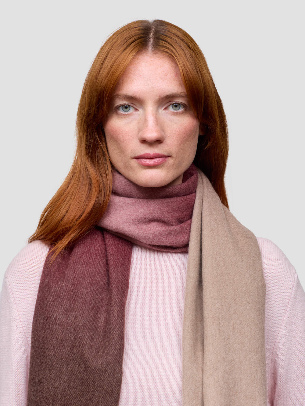 Woman wearing a pink cashmere sweater and a gradient cashmere scarf on a white background