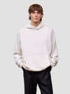 man wearing a white cashmere hoodie and black pants on a light gray background