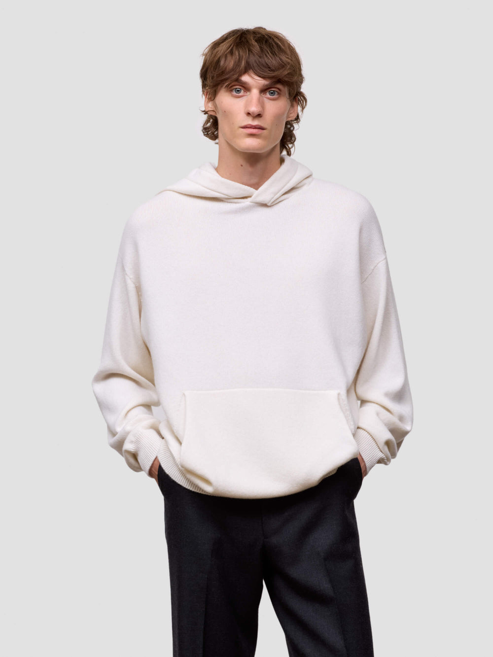 man wearing a white cashmere hoodie and black pants on a light gray background