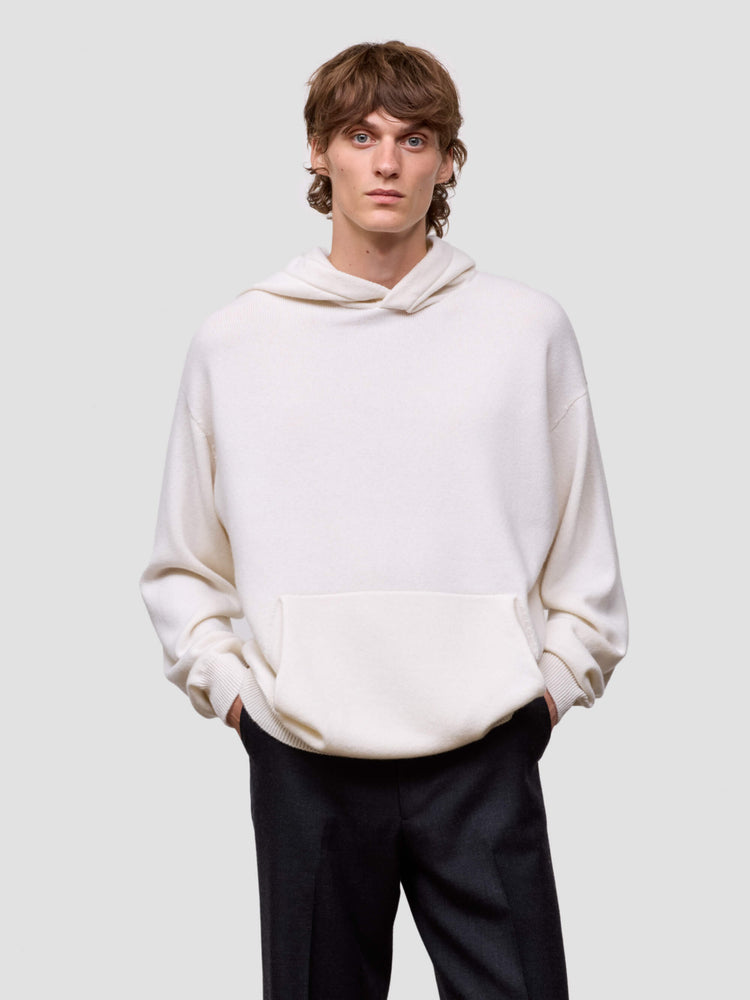 man wearing a white cashmere hoodie and black pants on a light gray background